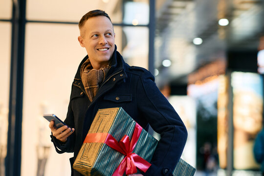 Happy man using smart phone while shopping for Christmas in city. - Powered by Adobe