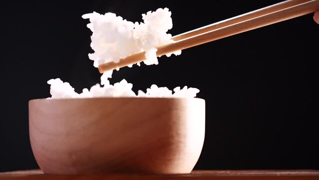 Japanese rice, Cook rice. Close up natural steaming cooked Japanese white rice in wooden bowl with chopstick on black background, soft focus. Healthy Food Concept.