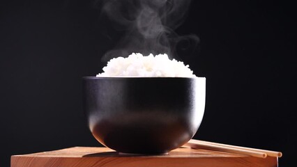 Japanese rice, Cook rice. Close up natural steaming cooked Japanese white rice in black bowl with chopstick on black background, soft focus. Healthy Food Concept.