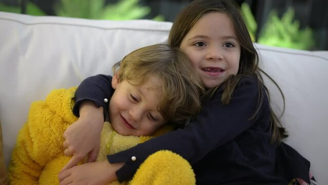Happy little siblings posing for camera. Child sister embracing small baby brother kissing on cheek. Family love and affection