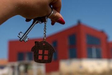 A woman's hand holds a house key against the backdrop of a house under construction. Real estate agent. Buying a house, apartment.