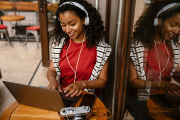 Young black woman in headphones using laptop in cafe indoors
