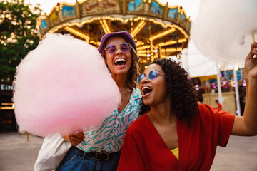 Young multiracial women eating cotton candy in attraction park