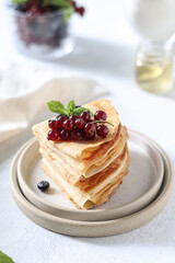 Thin pancakes in milk lie one on top of the other on a white plate, with berries and mint on top. Maslenitsa.