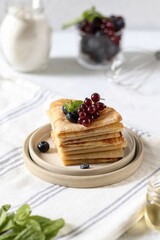 Thin pancakes in milk lie one on top of the other on a plate, with berries and mint on top. Maslenitsa.