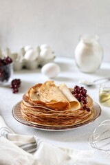 Thin pancakes with milk and eggs on a white table 