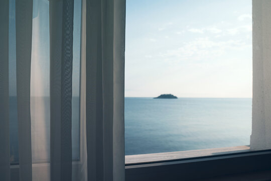 Fototapeta small ocean island seen through a window with transparent fabric curtains