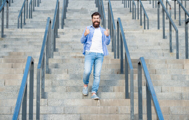 glad hipster walk downstairs. full length of hipster with beard. hipster man outdoor at stairs