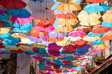 Catalina, Sicily, Italy. August 26, 2022. Multi colored umbrellas hanging amidst buildings with sky...