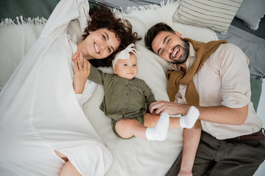 top view of happy parents and baby girl lying on bed at home.
