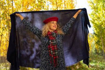 A young woman in the autumn forest, arms outstretched holding a large blue foulard behind her back.