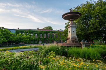 Obraz premium Green foliage around the fountain at the park in front of the old university building during summer in Lund Sweden
