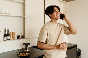 Asian young woman reading book and talking on cellphone in kitchen