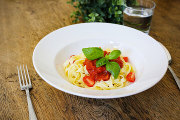 Lunch plate with tagliatelle pasta garnish with tomato and fresh basil with fork and spoon isolated on wooden table background. Top view.