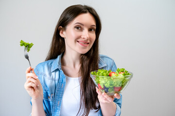 Happy beautiful young woman eats salad with lettuce, tomato and olives