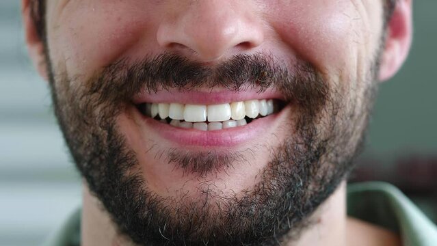 Selective focus on the lips of a handsome confident Caucasian bearded man, smiling a cheerful toothy smile standing forward to camera. White teeth, oral care, dental hygiene, teeth whitening concept