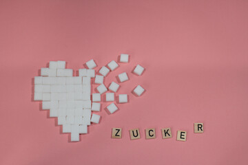 gebrochenes Herz aus Zuckerwürfel auf rosa Hintergrund mit dem Wort Zucker als Text