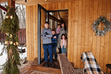 Obraz na płótnie Canvas Mother and kids in modern wooden house stand near door entrance.