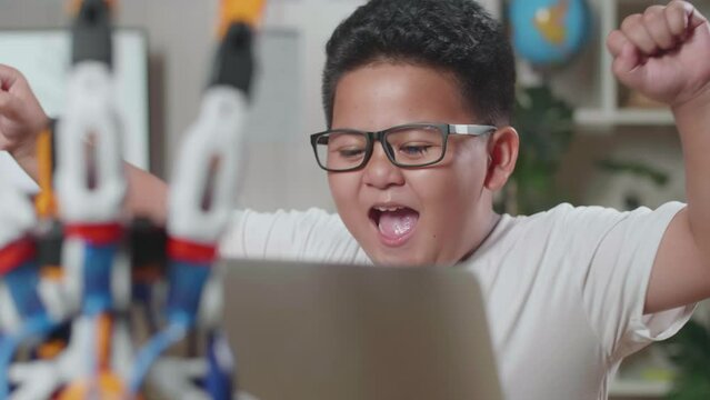 Close Up Of Asian Cute Boy Celebrating Succeed Working About A Cyborg Hand On A Laptop At Home
