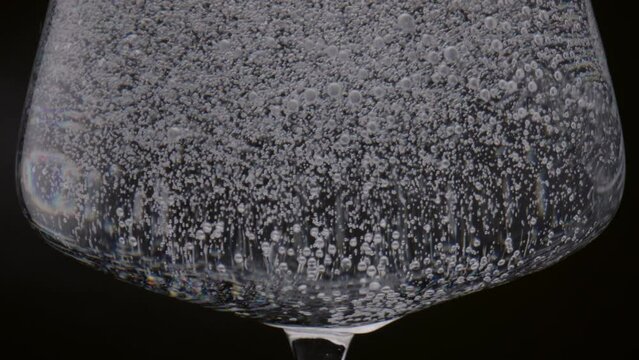 Glass filled fizzy water on black background close up. Sparkling drink in goblet