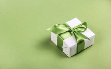 Obraz premium White gift box with green bow on green background. Gift box copy space