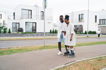 Black boyfriend helping girlfriend skate on street