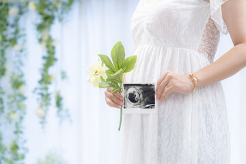 マタニティドレスでエコー写真を持つ妊婦...