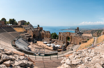 Panoramic view of old ruins of ancient Italian Teatro Antico di Taormina. Famous tourist attraction in Taormina. Historic building structure at Giardini Naxos bay on sunny day.