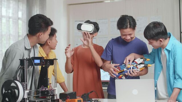 Group Of Young Asian Boys With 3D Printing And A Laptop Working At Home, Three Boys Enjoy Working On Metaverse While Two Boys Discussing About A Cyborg Hand 
