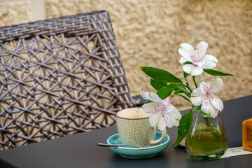 Cup of coffee next to a glass vase with white tropical flowers on a wooden table outside