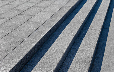 Fototapeta premium Gray steps of gray paving slabs. Gray concrete or stone stairs steps background. Abstract stairs, abstract steps, city stairs. Light and shadow on the stone steps. Black and white photography,diagonal