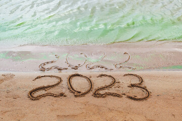 Top view of the sandy shore on which the numbers of the outgoing year 2022 are drawn, which were almost washed away by a wave of green water, and the clear numbers of 2023 of the new coming year.