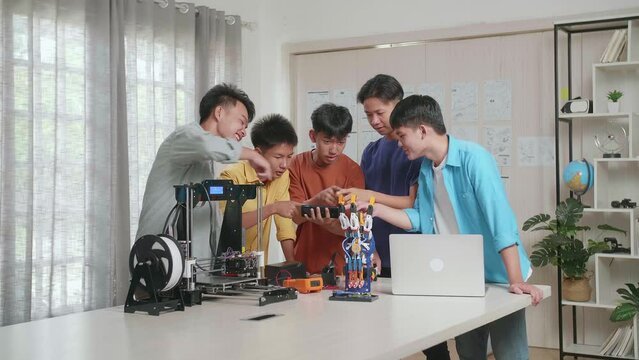 Group Of Young Asian Boys With A Laptop And 3D Printing Comparing A Cyborg Hand To The Pictures On Smartphone While Working At Home
