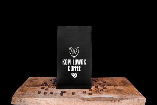 Kopi Luwak coffee beans and black package on wooden board with black isolated background