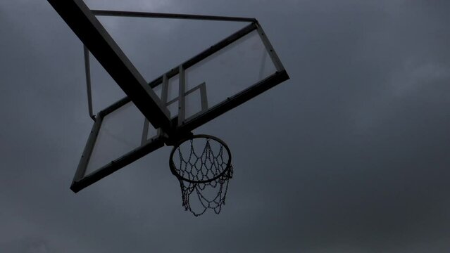 Time lapse of a basketball rim with a shot taken from below the chain rim on a cloudy day with the sky dancing in the background