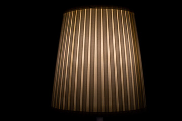 Lampshade lamp. Lamp is in dark. Light on black background. Ribbed paper.