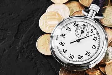 Analog stopwatch and pile of gold coins on a black background close-up. Counting time by stopwatch. Time measurement. Time management concept.A tool for measuring time.Dial stopwatch arrow