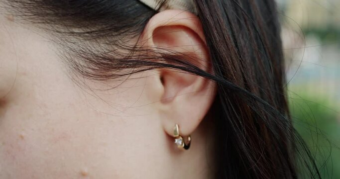 Close-up of woman ear wearing elegant earring. Listen sound or music ear CU. Female with long black hair during windy weather. She is wearing head accessory and jewelry.