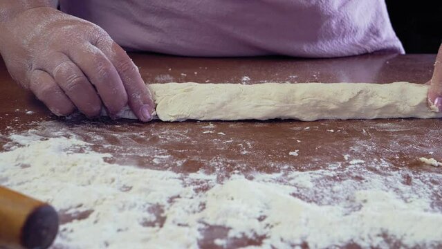 The hands of a Jewish woman form dough pieces for challah on the table. Medium plan