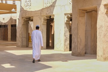 Rear view on unidentified Arabic man wearing white traditional middle eastern clothes walking in the old city.