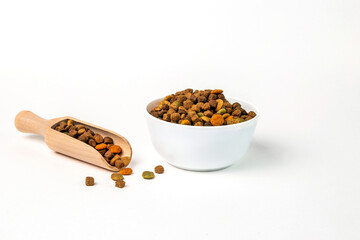 A bowl full of dry pet food, and a scoop full of food on a white background.