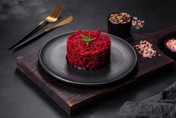 Cooked grated beetroot formed as a cylinder and ready dish on a black plate