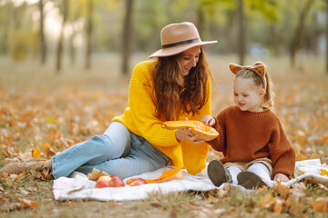 Fall picnic with pumpkin. Young mother and cute daughter resting in nature. Autumn harvest....