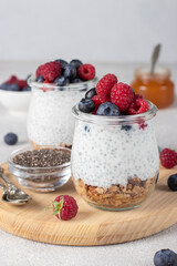 Chia pudding with muesli, fresh berries, honey and natural yogurt on wooden board on gray table....