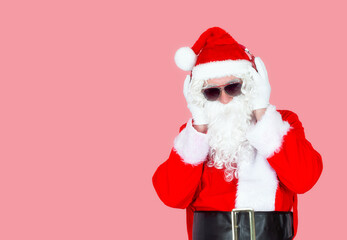 Portrait of a gray-haired old man in a Santa Claus costume with headphones, enjoy a modern Christmas show at a party, isolated pink background