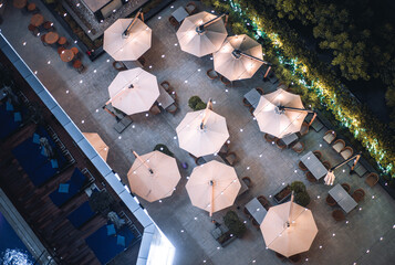 A night top view of an esplanade of a resort cafe or a restaurant with sunshade umbrellas, tables...