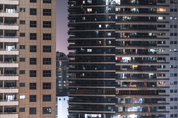 Fototapeta na wymiar Facades of two big residential houses, high-rises at night with illuminated windows and pink sky in the background; elevation of two dwelling skyscrapers with dark and bright windows and balconies