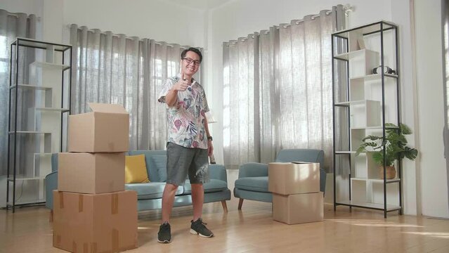 Asian Man With Cardboard Boxes Smiling And Showing Thumbs Up Gestures To Camera In The New House
