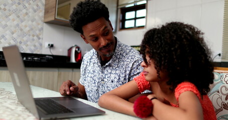Black father helping daughter with computer laptop at home kitchen