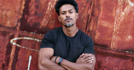 Bad boy African man crossing arms staring at camera in urban grunge background